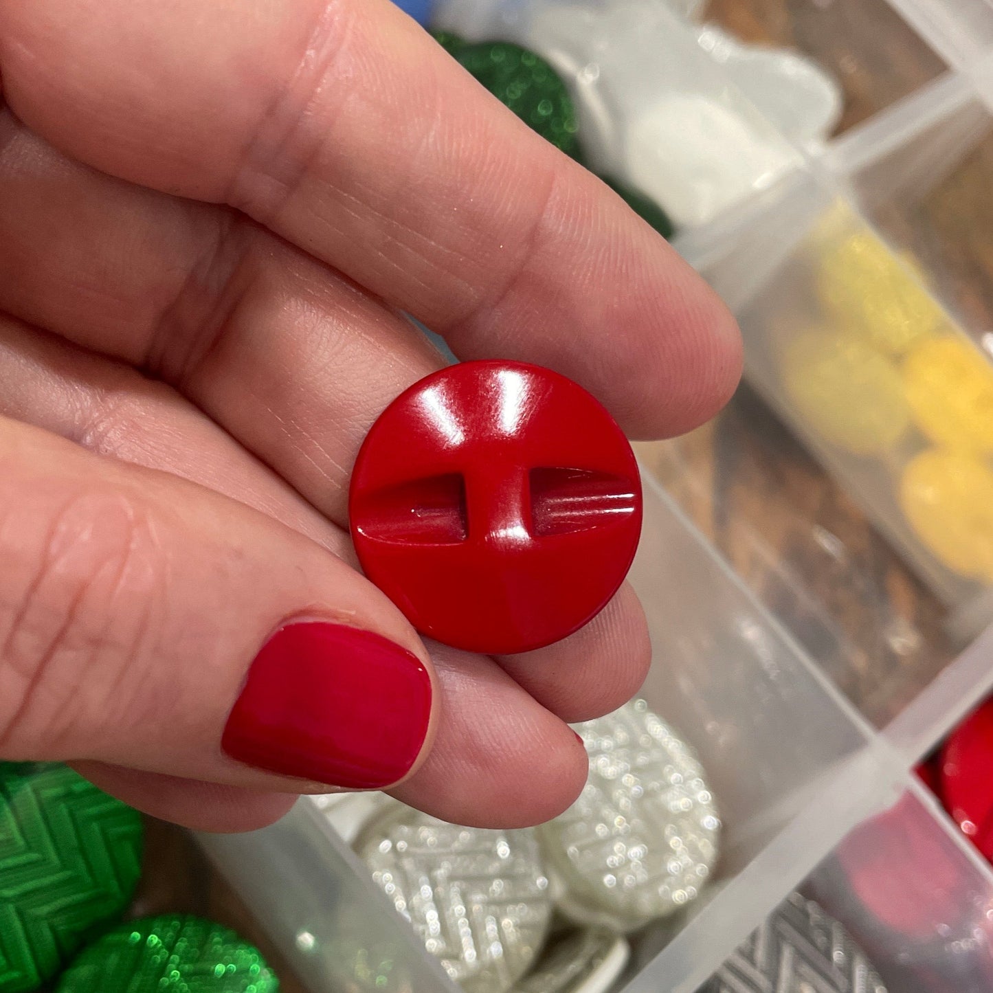 Hand holding a red button with a container of various buttons in the background