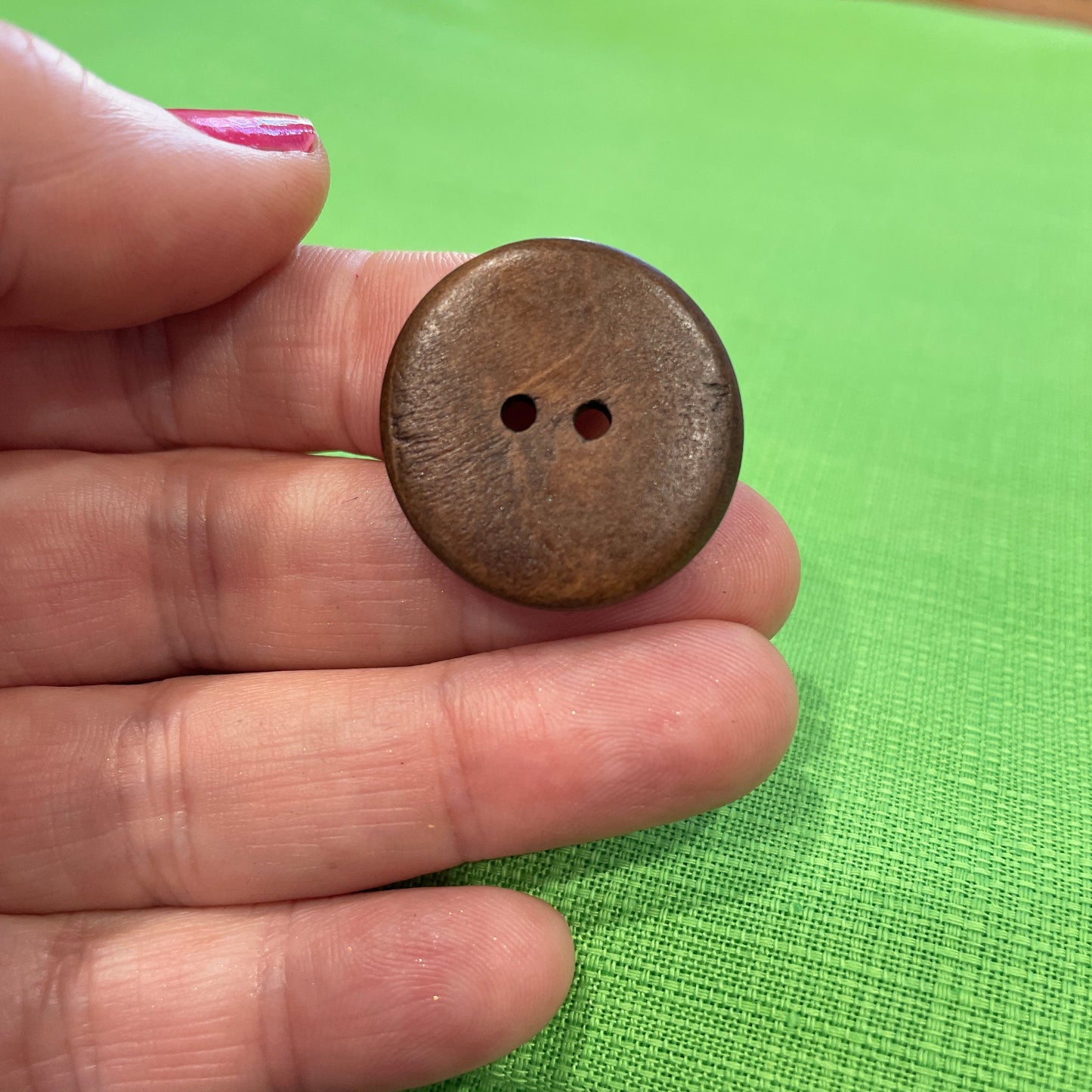 Brown button held between fingers against a green fabric background