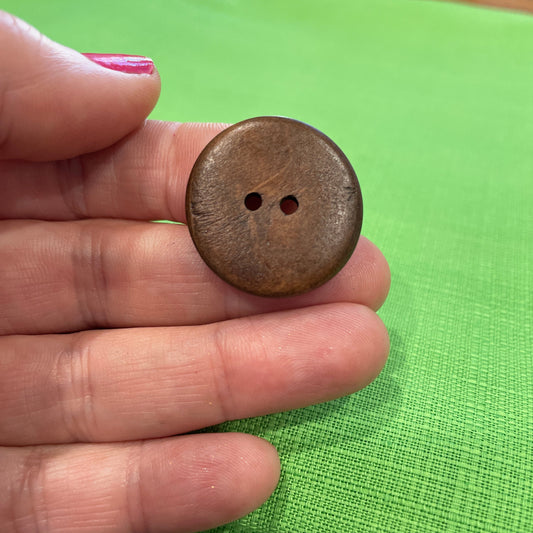 Brown button held between fingers against a green fabric background