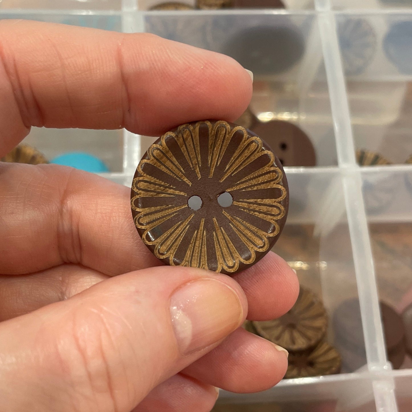 Hand holding a decorative button with a clear container of assorted buttons in the background