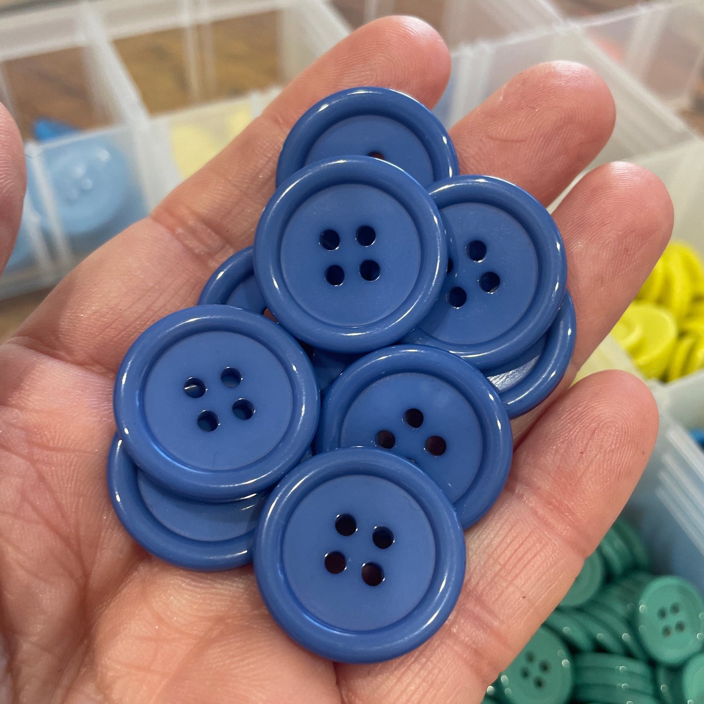 Hand holding blue buttons with a blurred background of more buttons and containers.