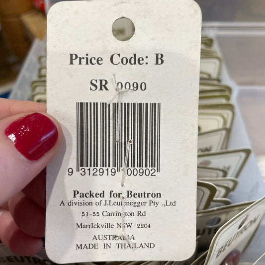 Close-up of a product tag with a barcode and text, held by a hand with red nail polish.