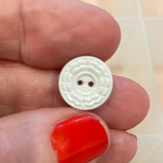 Hand holding a white button with a background of various buttons in a box.