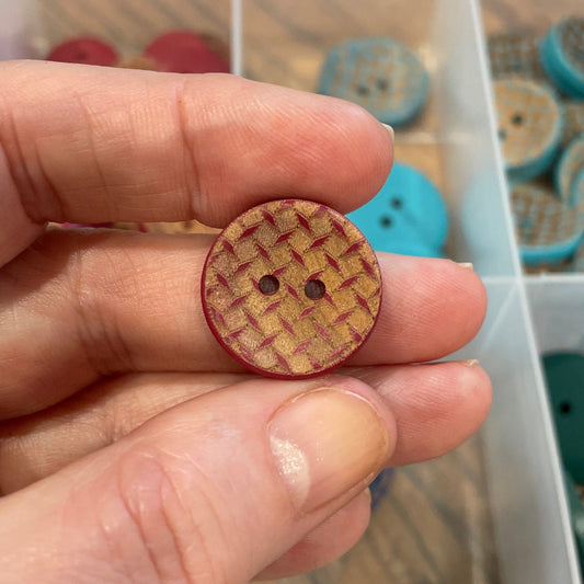 Hand holding a wooden button with a background of a button organizer.