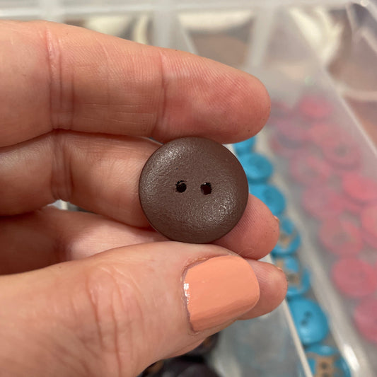 Brown button held between fingers with a container of buttons in the background