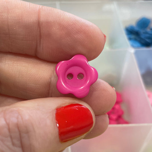 Hand holding a pink button with a blurred background of colorful buttons