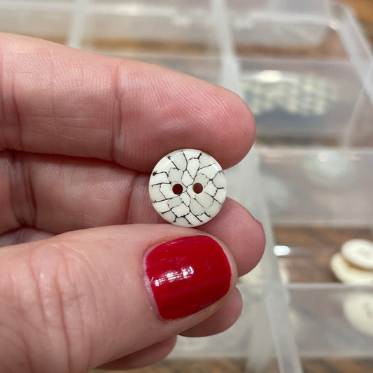 Close-up of a hand holding a small decorative button with a red center, against a blurred background of similar buttons.