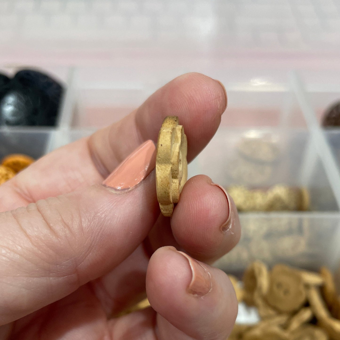 Hand holding a gold coin with a container of buttons in the background