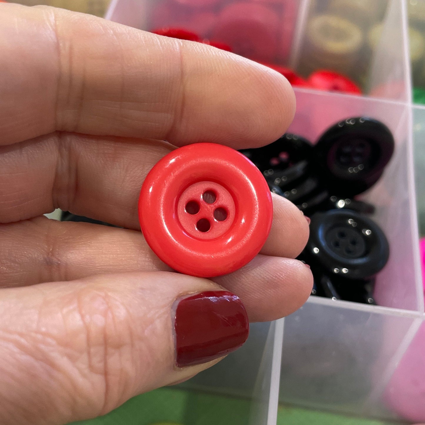 Hand holding a red button with a container of assorted buttons in the background