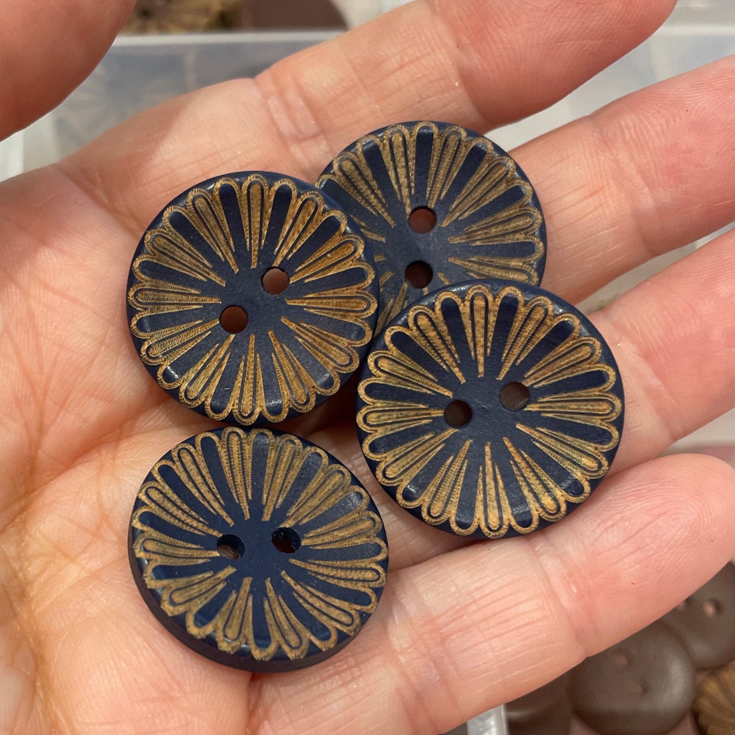 Hand holding three decorative buttons with a clear container of buttons in the background