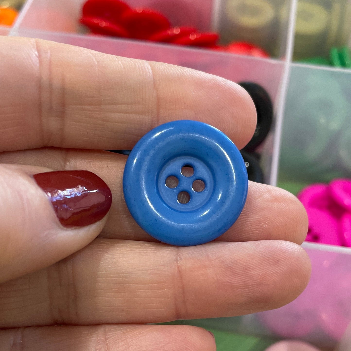 Hand holding a blue button with a container of colorful buttons in the background
