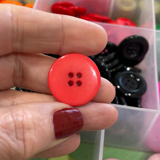 Hand holding a red button with a container of colorful buttons in the background