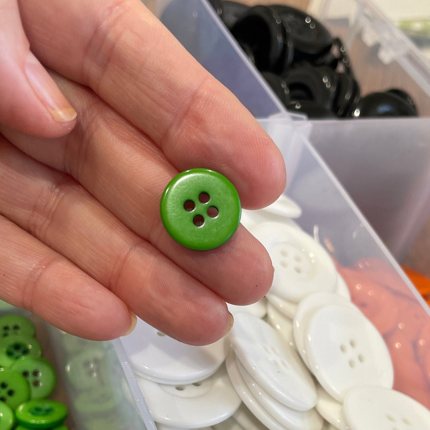 Hand holding a green button with a container of buttons in the background