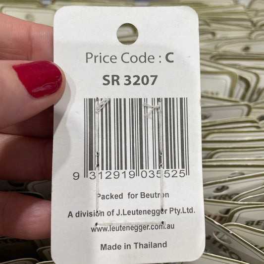 Close-up of a product tag with a barcode and text, held by a hand with red nail polish.