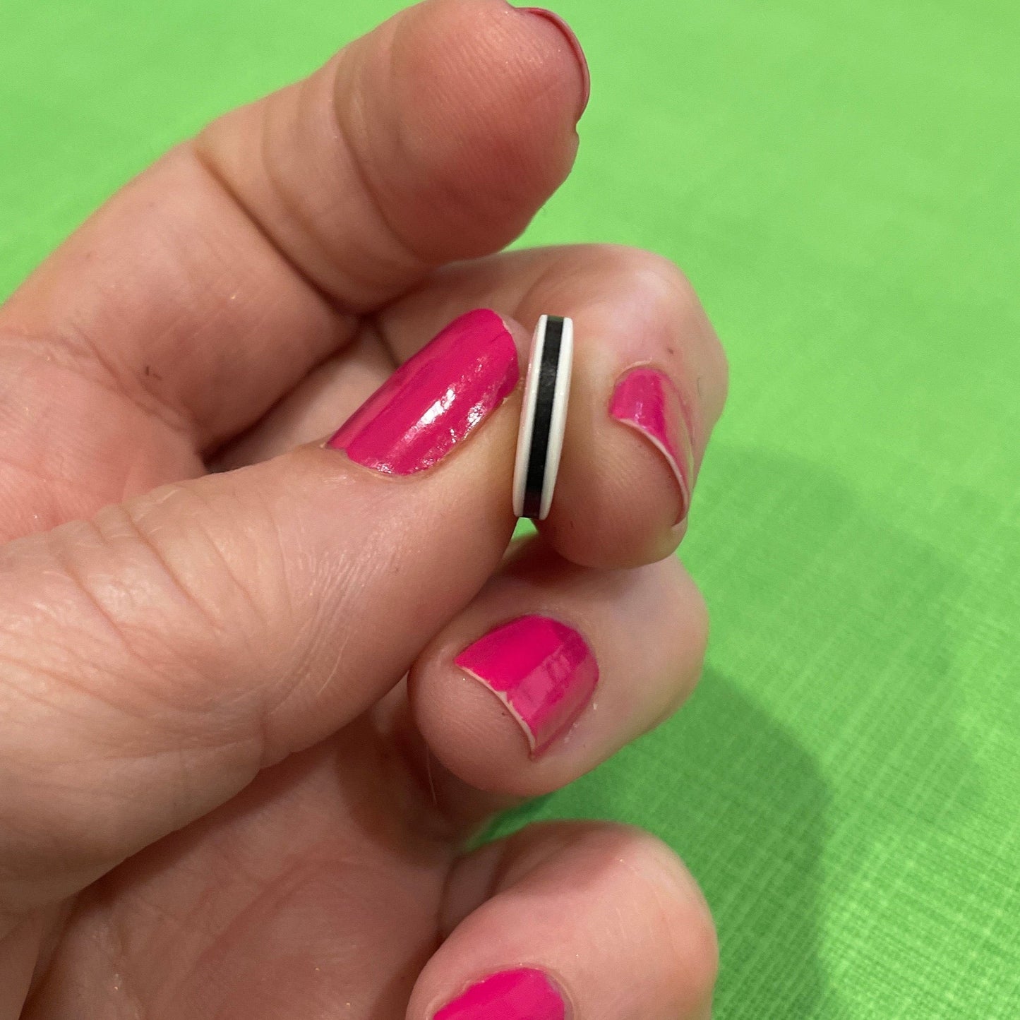 Hand with pink nail polish holding a small object against a green background