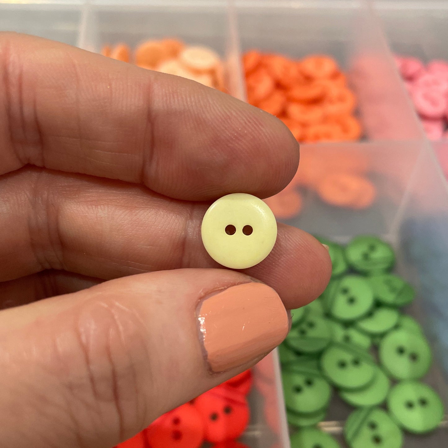 Hand holding a yellow button with a container of colorful buttons in the background