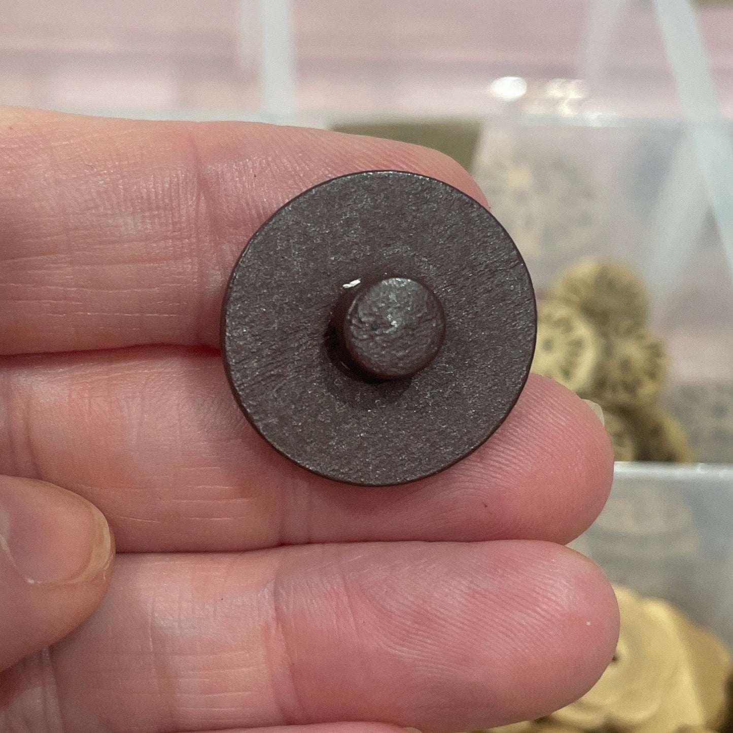 Hand holding a button with a background of button collection in a box.