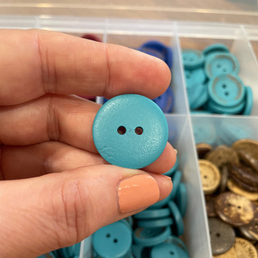 Hand holding a blue button with a container of buttons in the background
