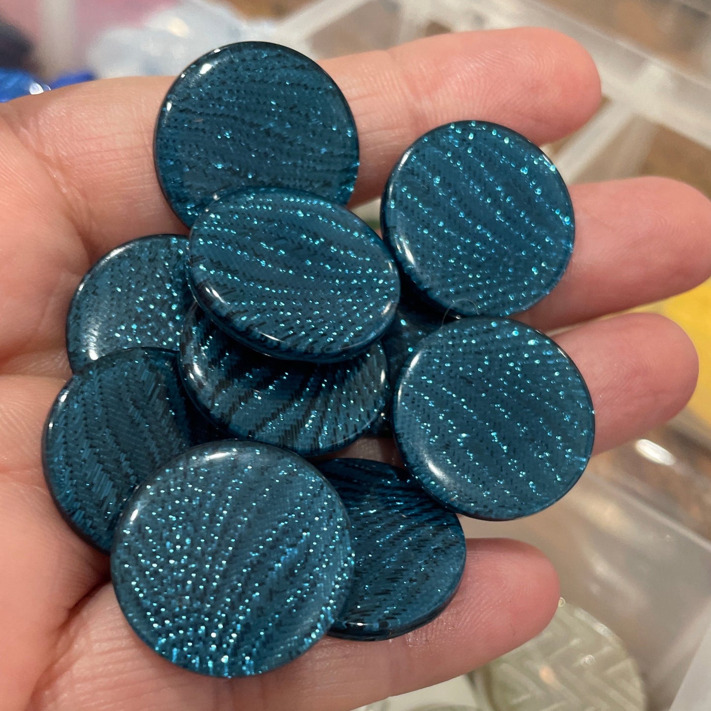 Hand holding blue circular objects with a container of similar objects in the background
