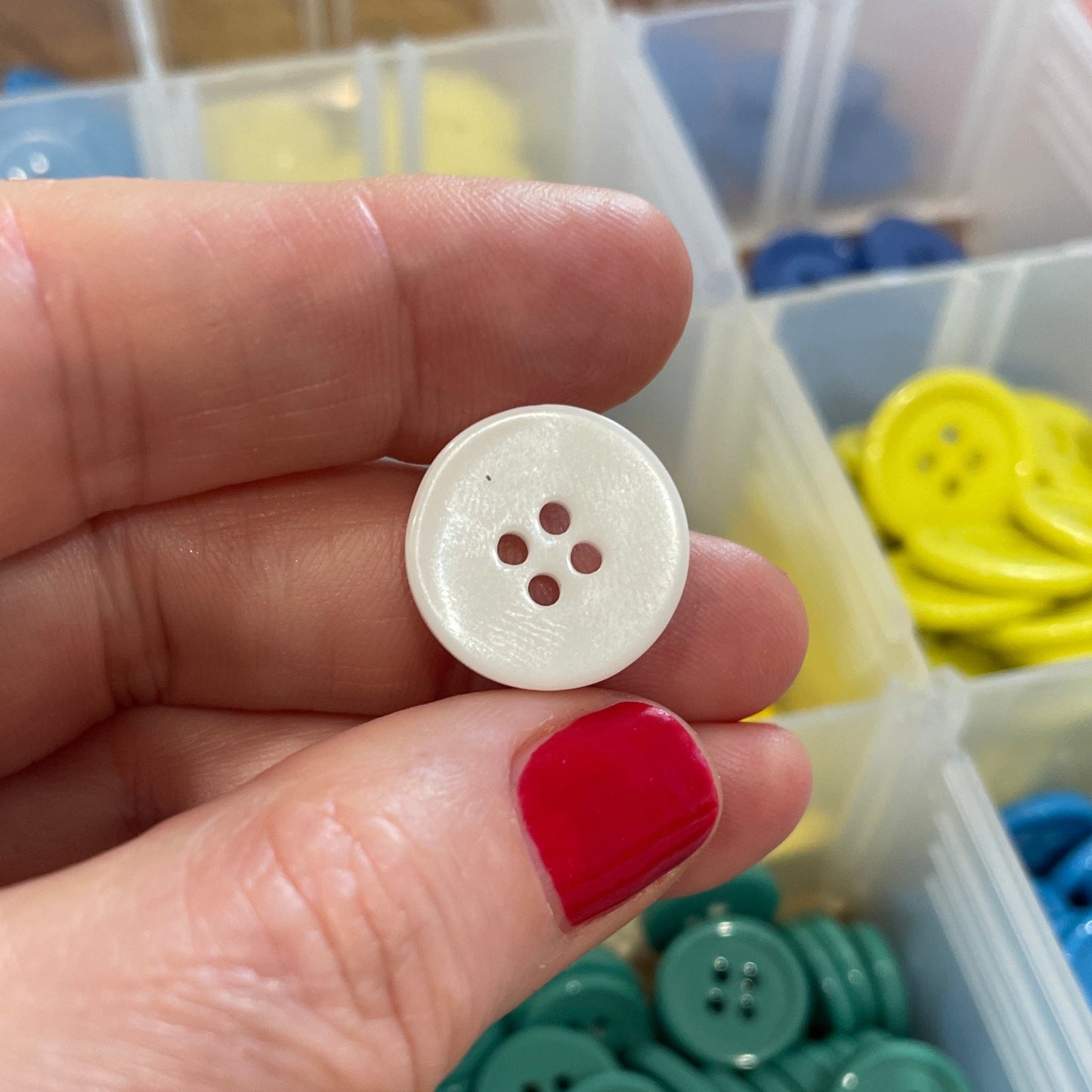 Hand holding a white button with a container of colorful buttons in the background
