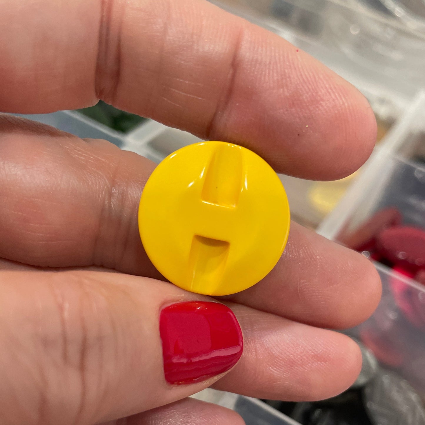 Hand holding a yellow button with a blurred container of buttons in the background