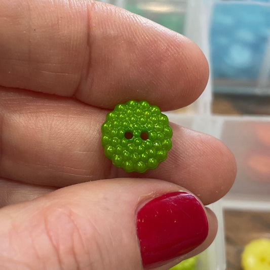 Green button held between fingers with a container of buttons in the background