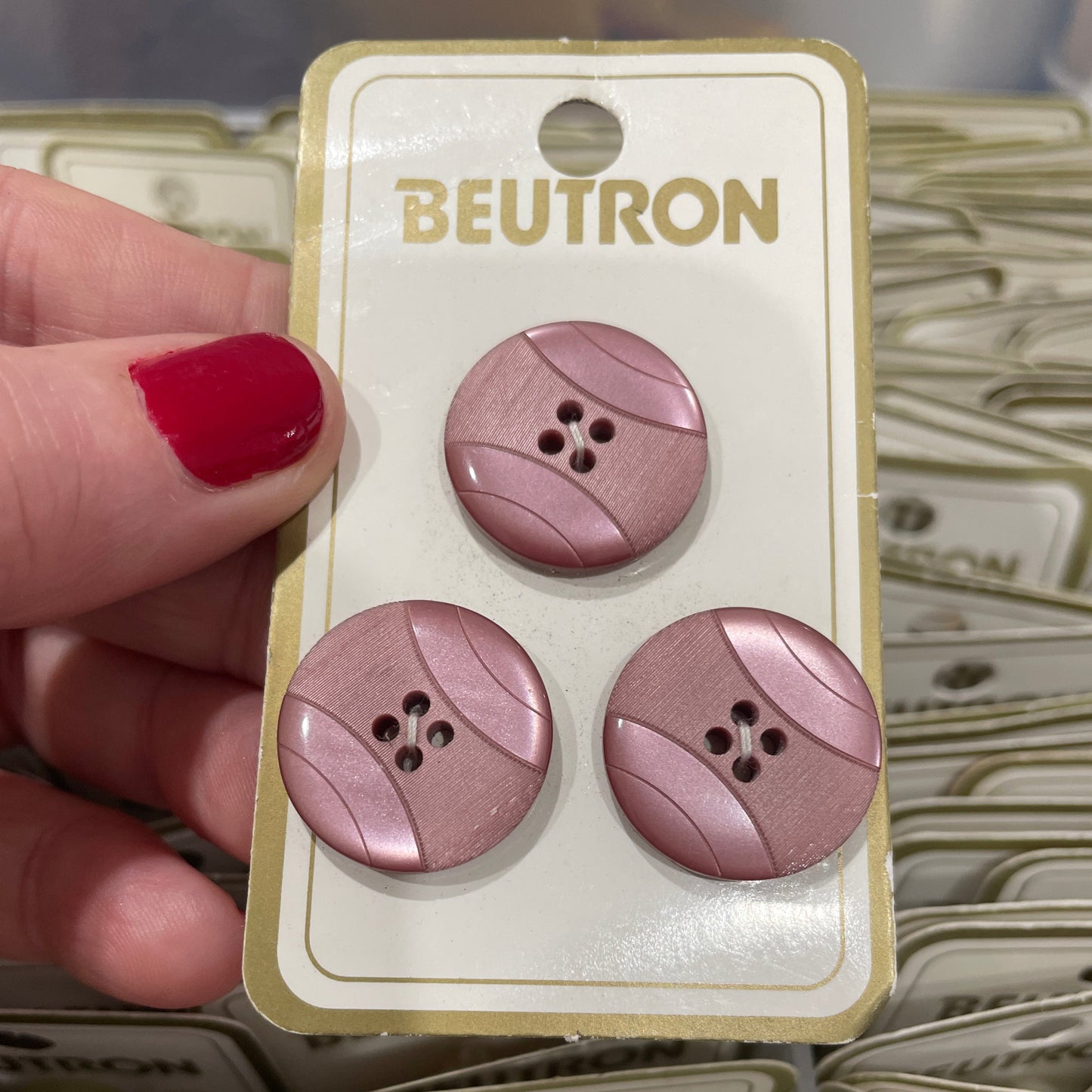 Three purple buttons on a Beutron card held by a hand with red nail polish.