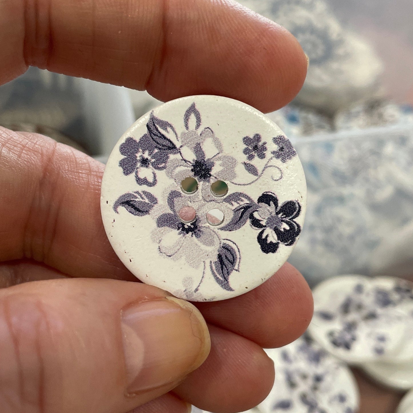 Hand holding a floral-patterned button with a blurred background of more buttons.