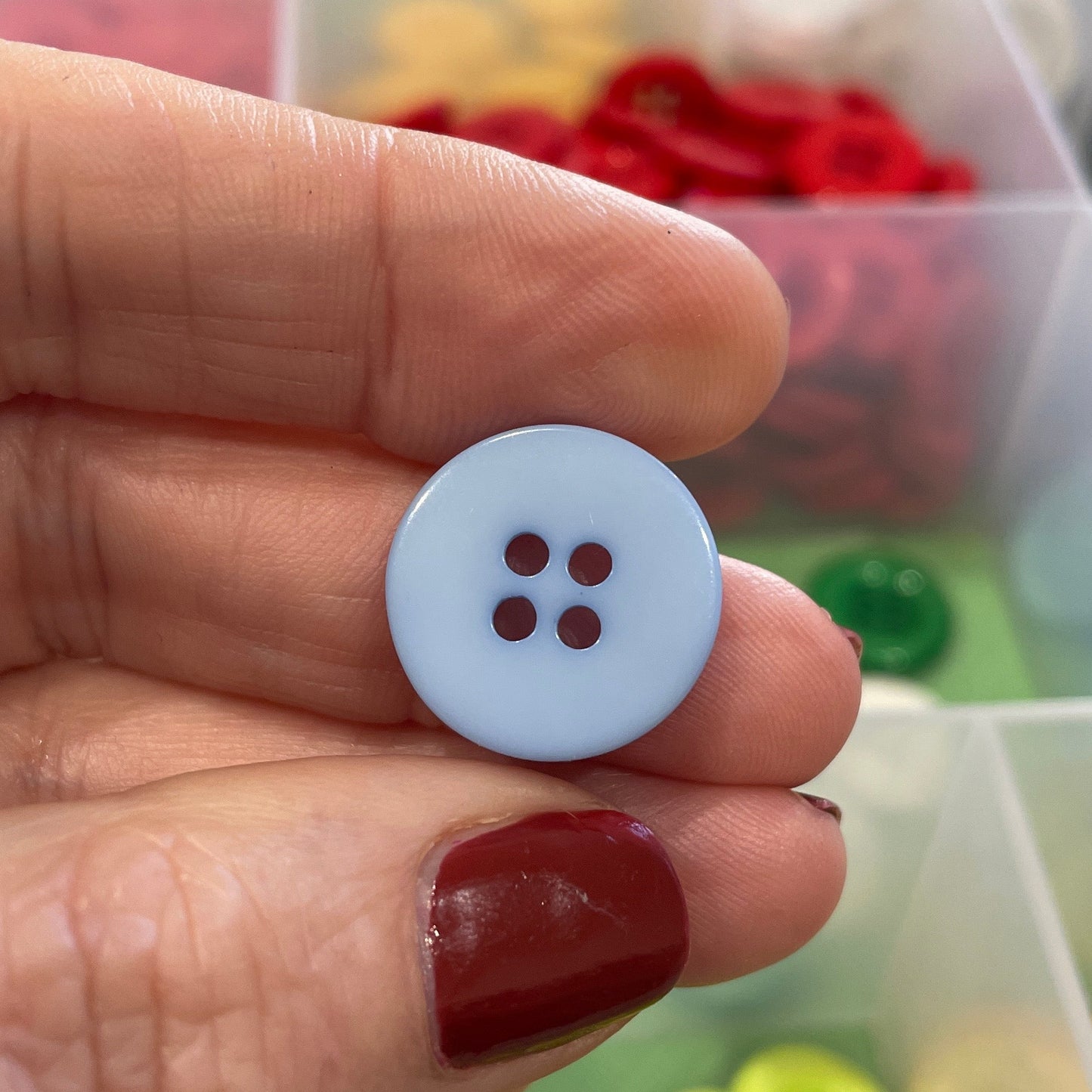 Hand holding a white button with four holes against a background of colorful buttons.