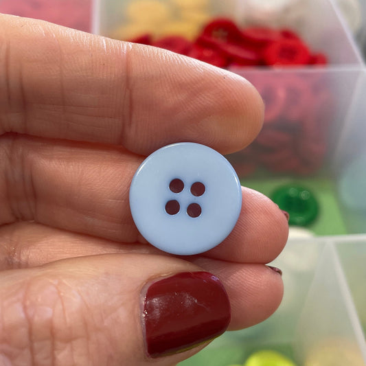 Hand holding a white button with four holes against a background of colorful buttons.