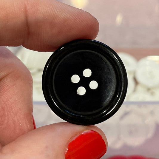 Black button held by a hand with a container of buttons in the background