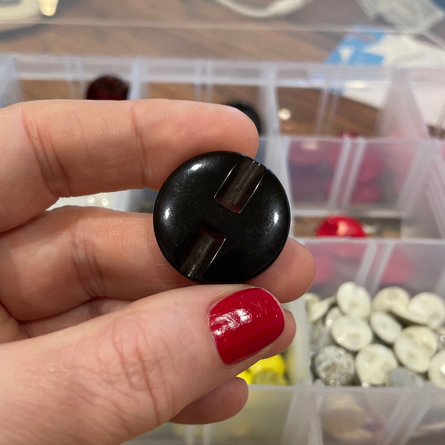 Hand holding a black button with a container of colorful buttons in the background