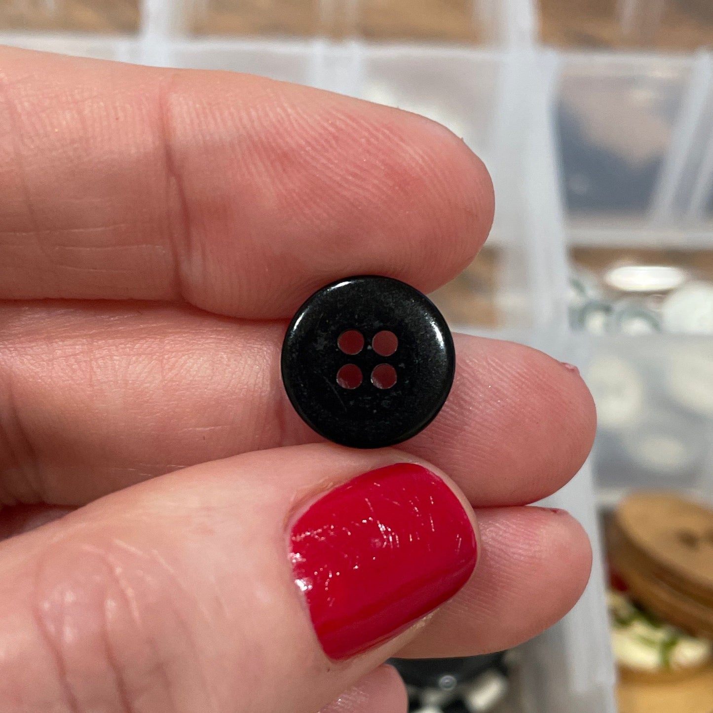 Hand holding a small black button with a container of buttons in the background