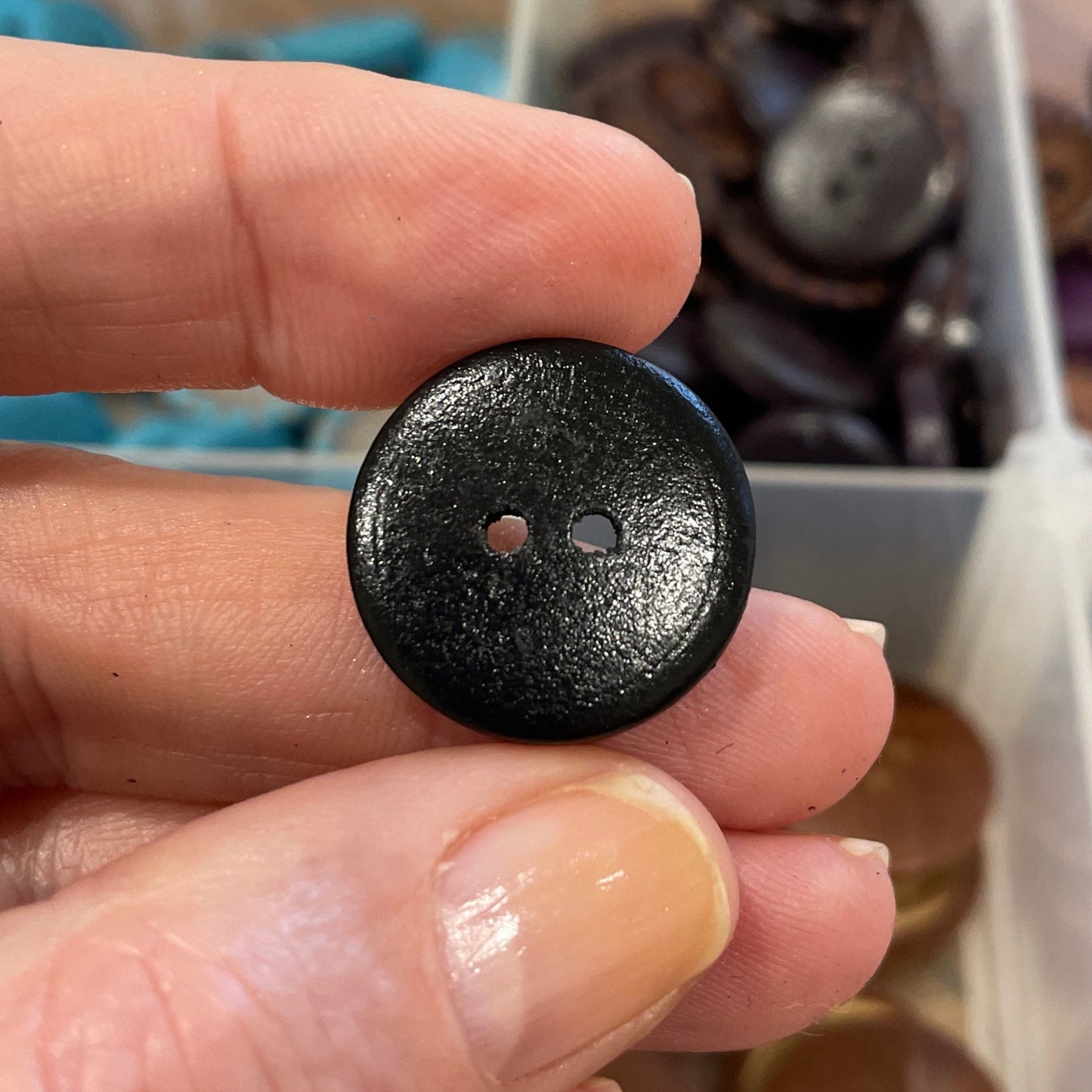 Hand holding a black button with a collection of buttons in the background
