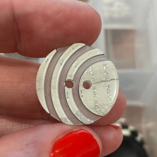 Hand holding a round wooden button with a blurred background of button collection