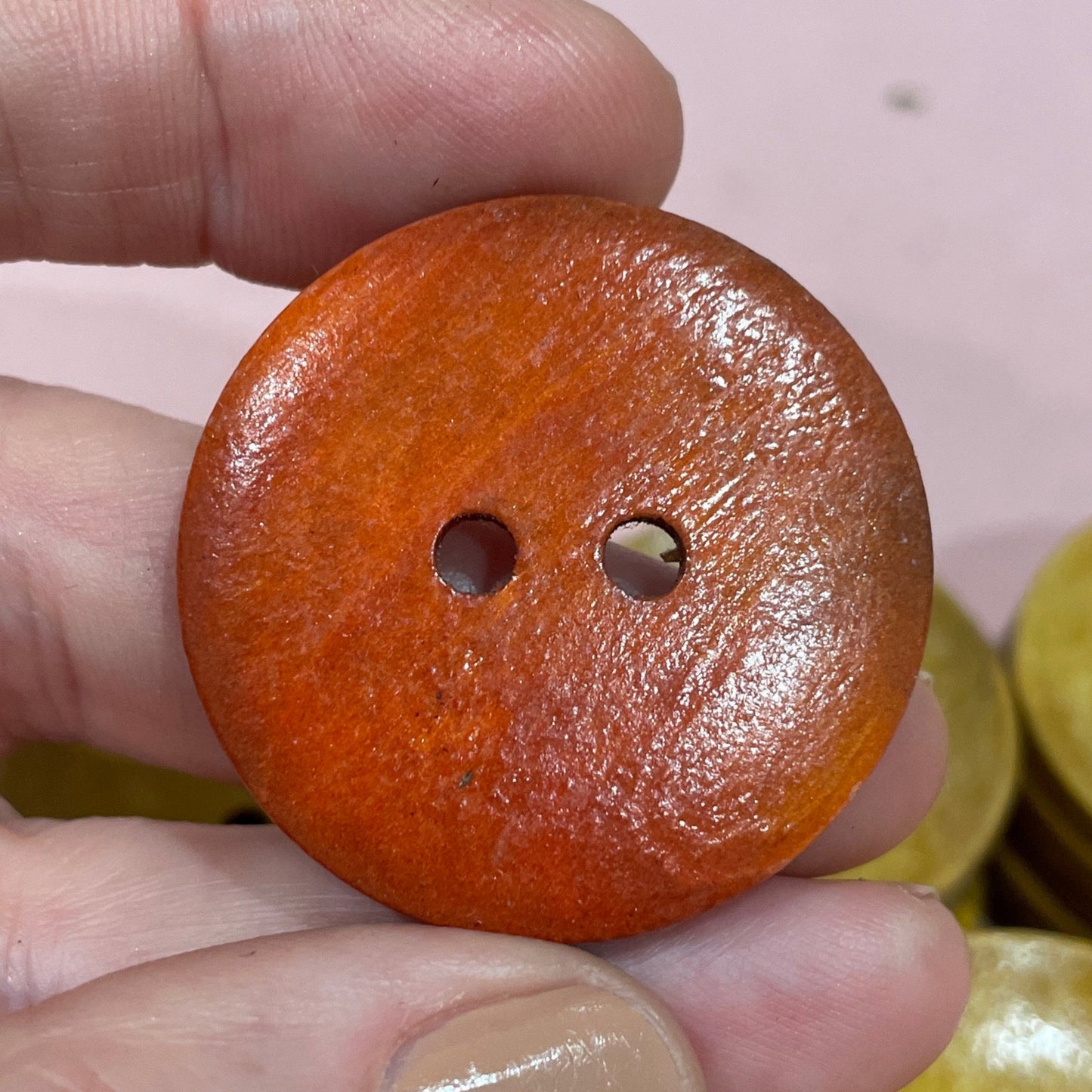 Hand holding a brown button with other buttons in the background on a pink surface