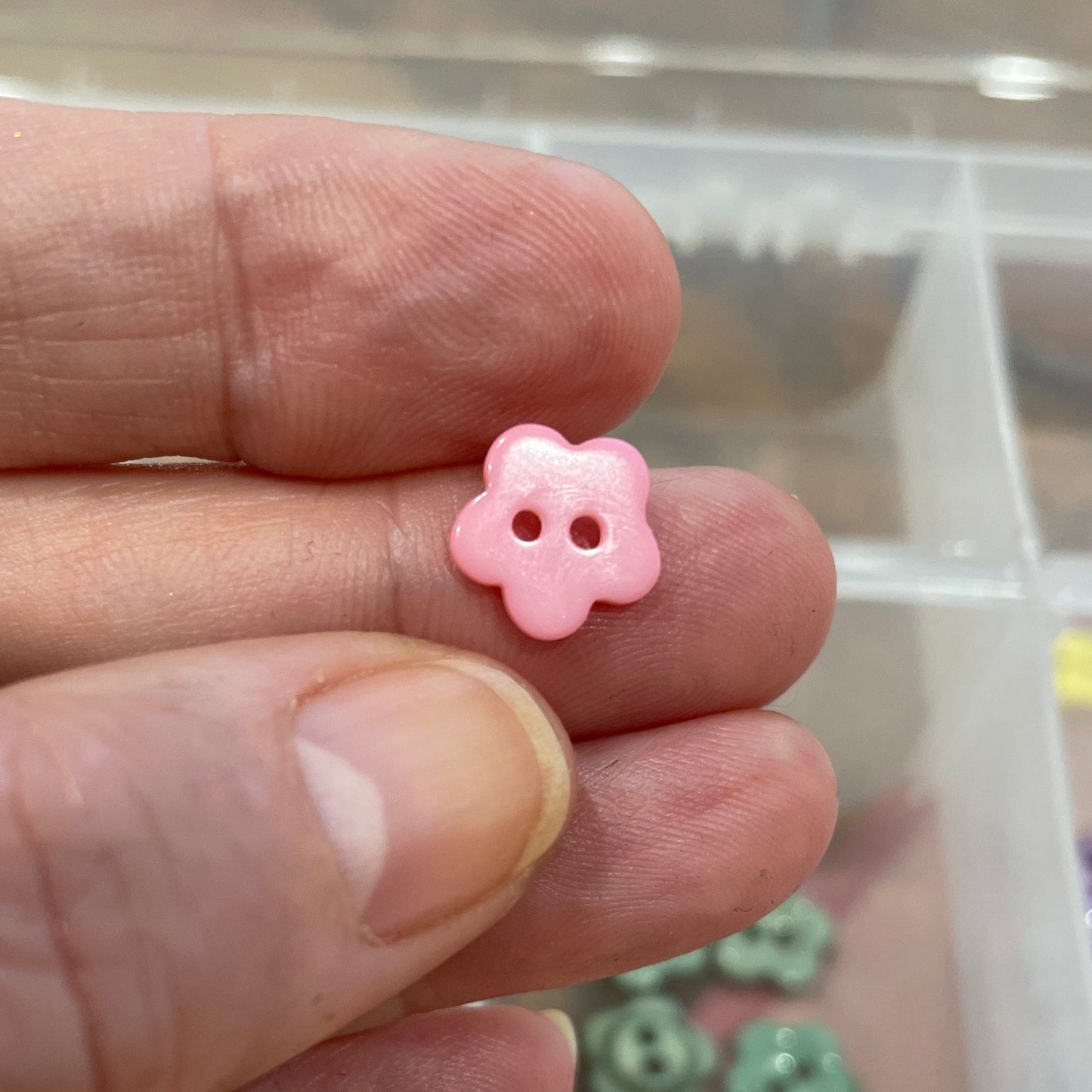 Hand holding a pink flower-shaped button with a blurred background of colorful buttons.