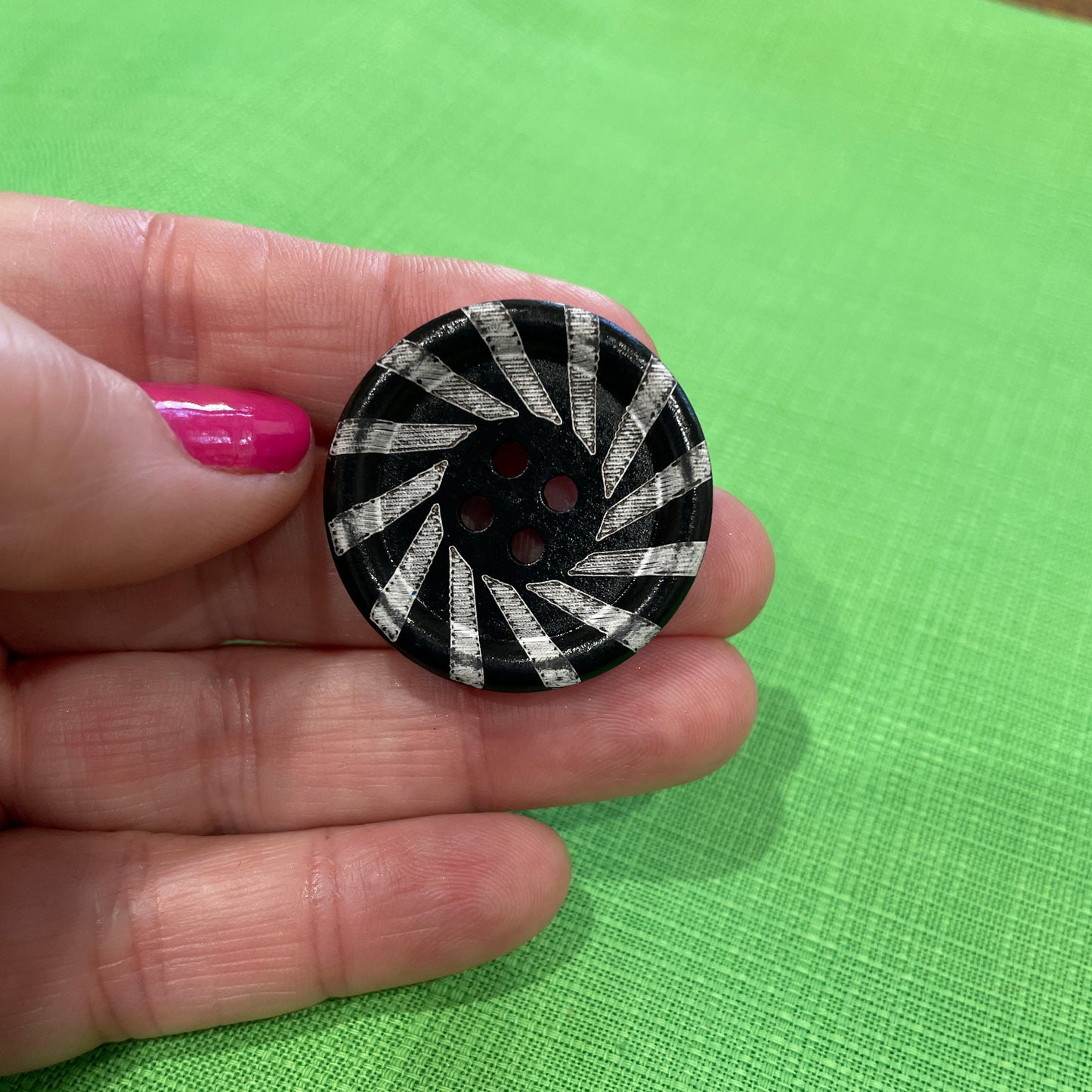 Hand holding a black and white patterned button against a green background