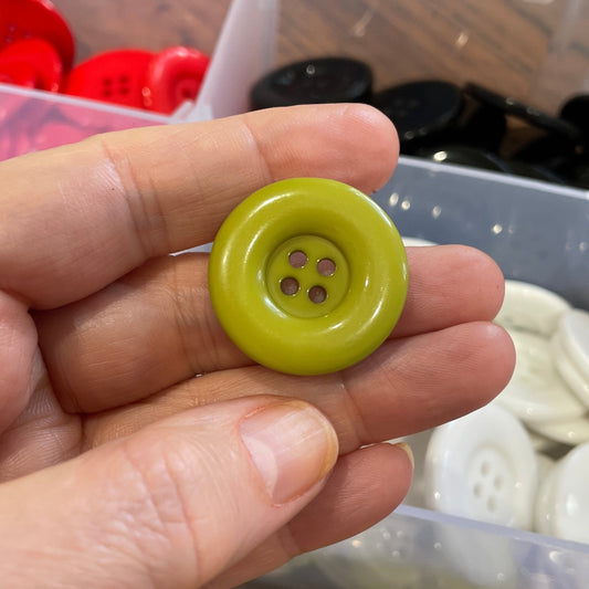 Hand holding a green button with a container of buttons in the background