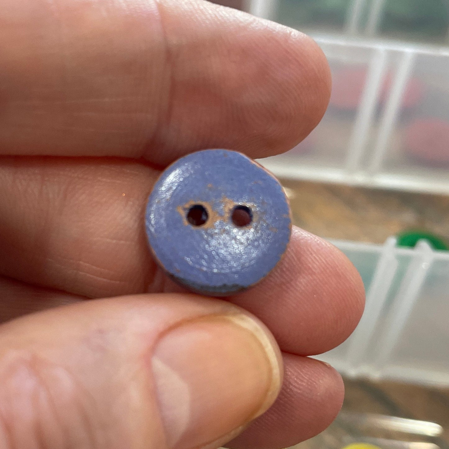 Hand holding a small purple button with a clear container of buttons in the background