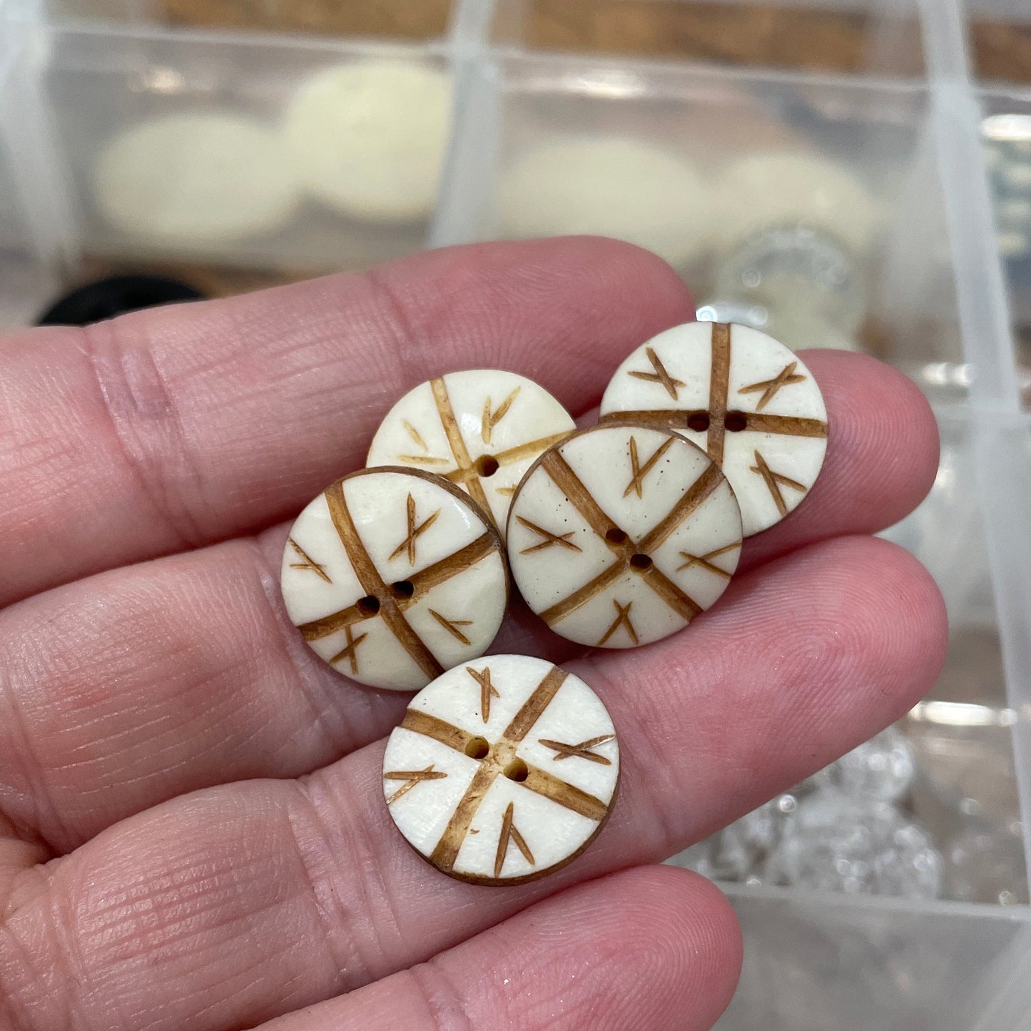Hand holding four round wooden buttons with gold patterns against a blurred background of more buttons.
