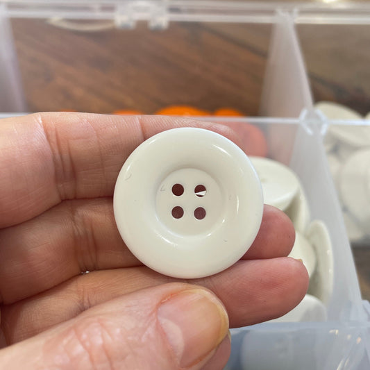White button held by a hand with a clear container of buttons in the background