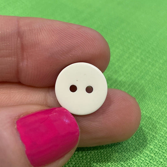 Small white button held between fingers against a green background