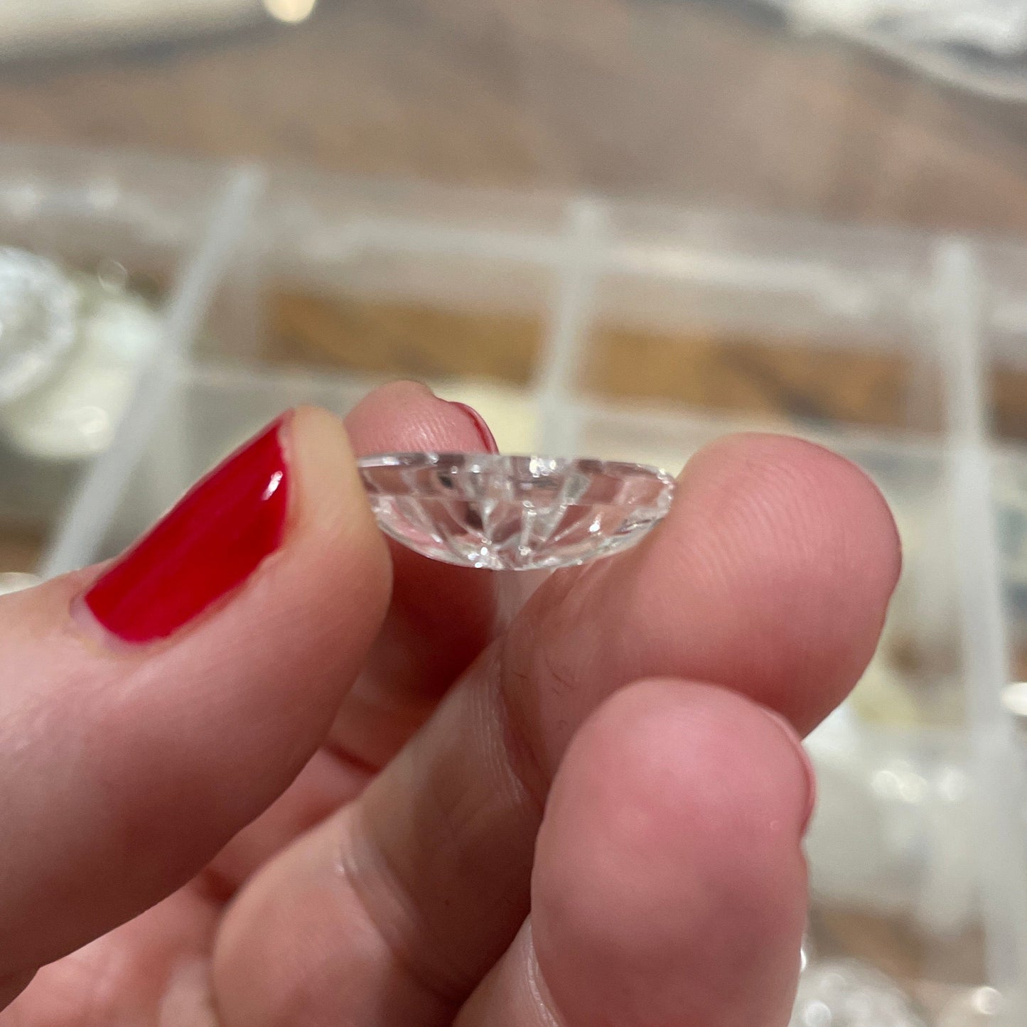 Hand holding a clear gemstone with a blurred background of jewelry display cases.