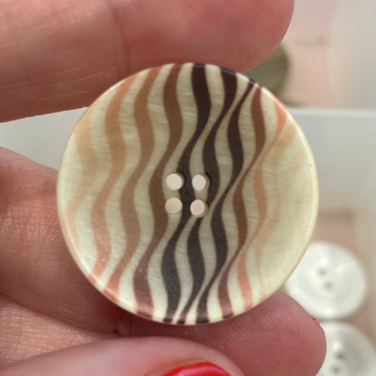 Hand holding a button with zebra pattern against a background of various buttons