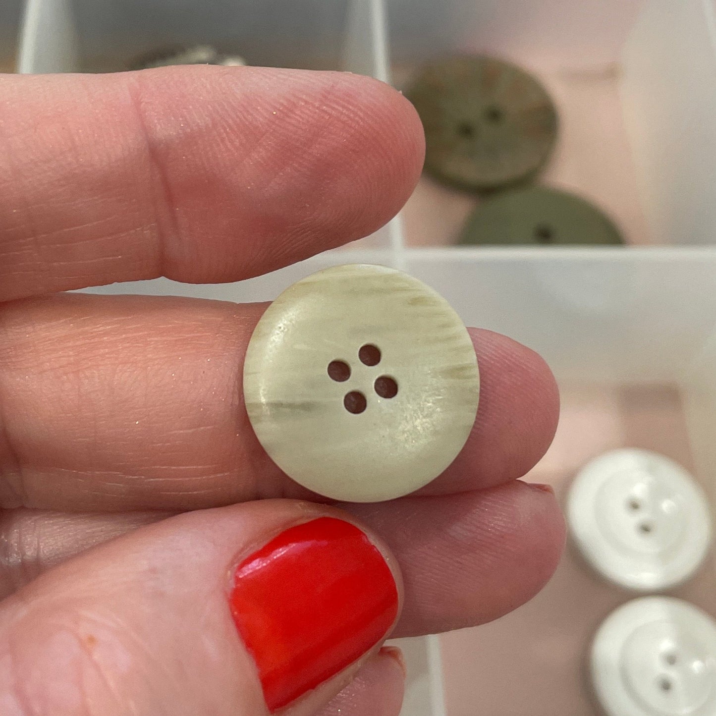 Hand holding a beige button with a clear container of buttons in the background