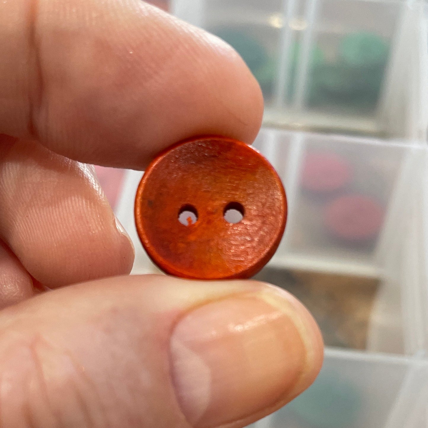 Hand holding a brown button with a clear container of buttons in the background