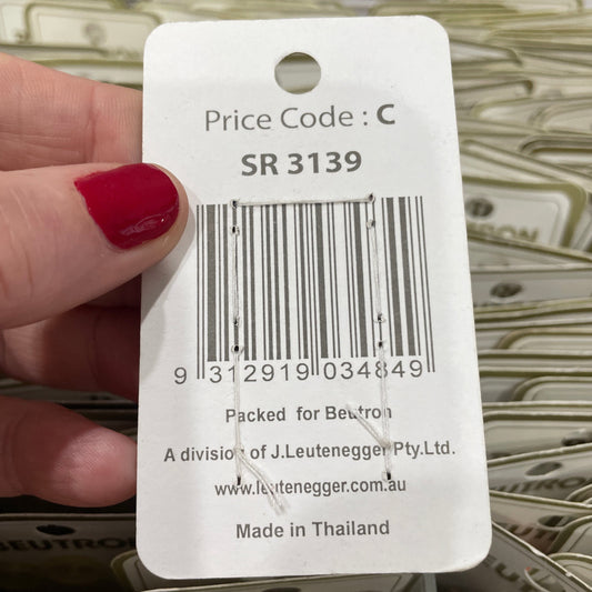 Hand holding a product tag with a barcode and text, blurred background