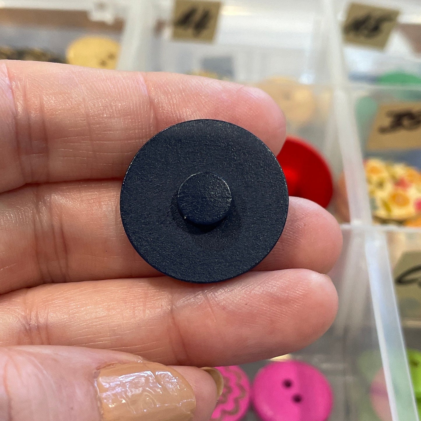 Hand holding a black button with a background of colorful buttons in a container