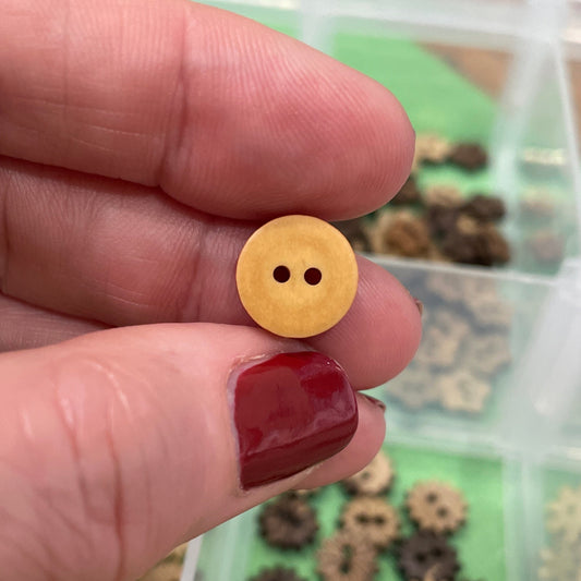 Hand holding a small yellow button with a blurred background of buttons.